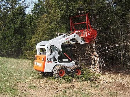 A Bobcat skid steer with a forestry mulching head clearing brush in a field — reference photo, not JKE's own machine