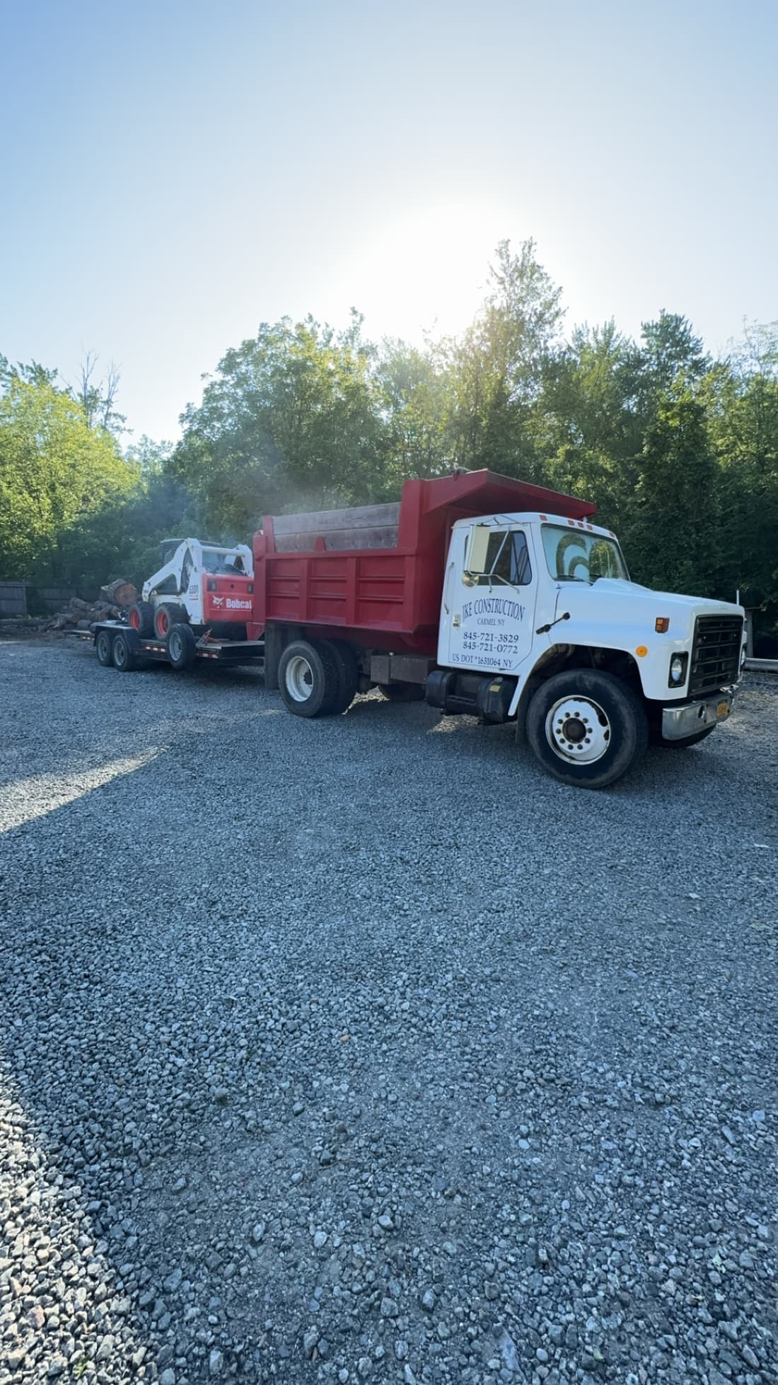 JKE Construction dump truck towing a trailer with a Bobcat skid steer and cut logs at a job site