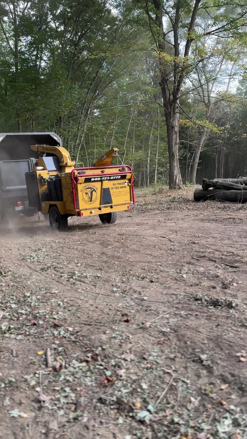 JKE's tracked wood chipper working at the edge of a wooded lot, with cut logs stacked nearby